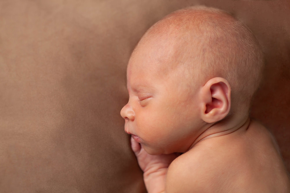 Profile of sleeping baby boy on a brown background