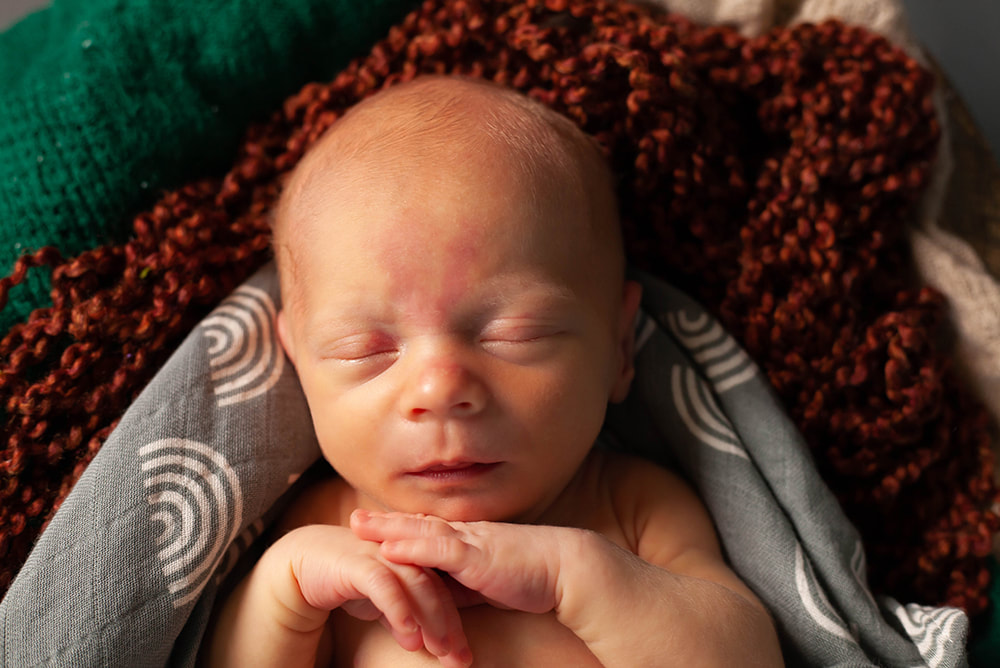 Close up of sleeping newborn baby boy on jewel toned blankets
