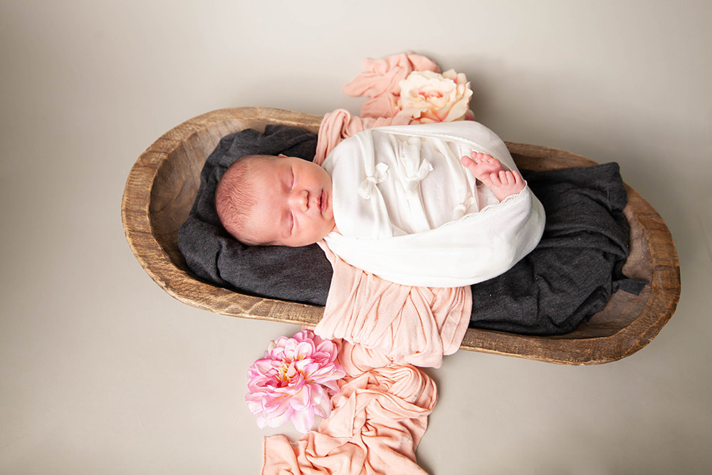 Swaddled baby girl sleeping in a long wooden bowl in theTampa Bay Area 