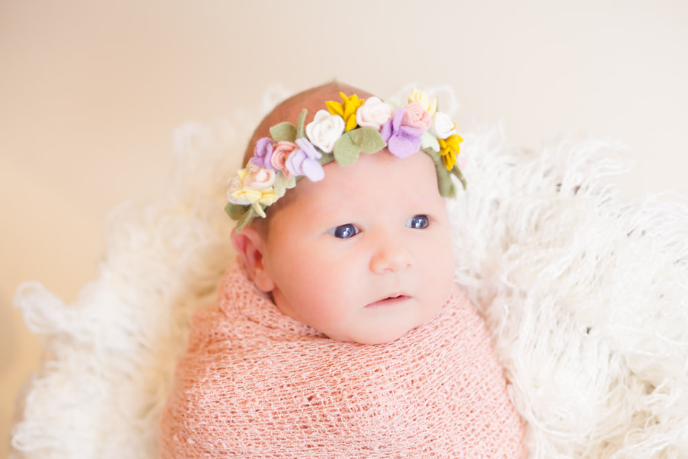 Wide awake newborn baby swaddled in pink with a flower headband on