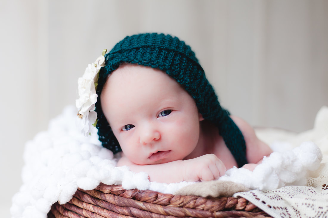 Newborn baby girl in Lutz looks into camera while wearing an emerald green knit outfit