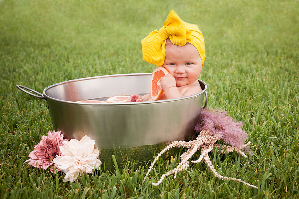 baby in metal tub holding a slice of grapefruit with big yellow turban on her head