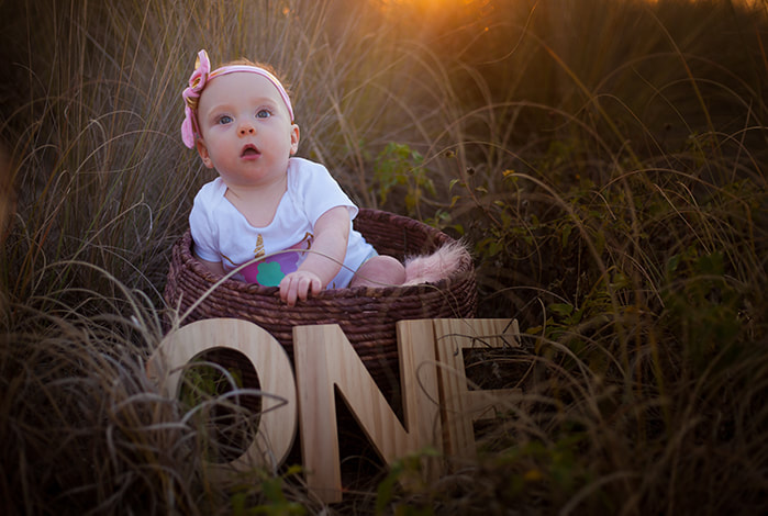One year old baby in basket nestled in tall grass with a dreamy feel