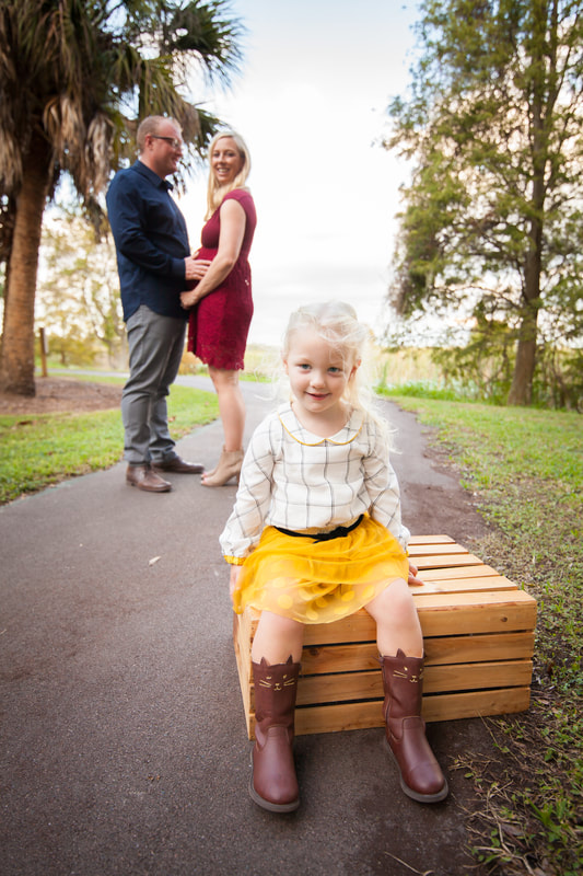 Smiling little girl about to become a big sister sits with her parents behind her