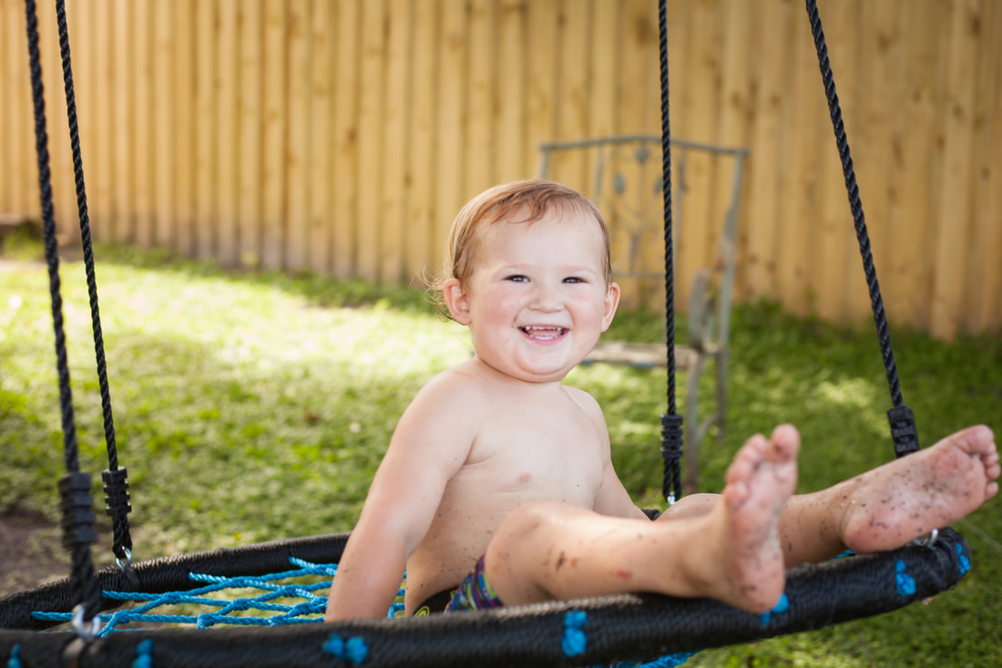 Two year old smiles at camera while swinging on swing in Temple Terrace FL