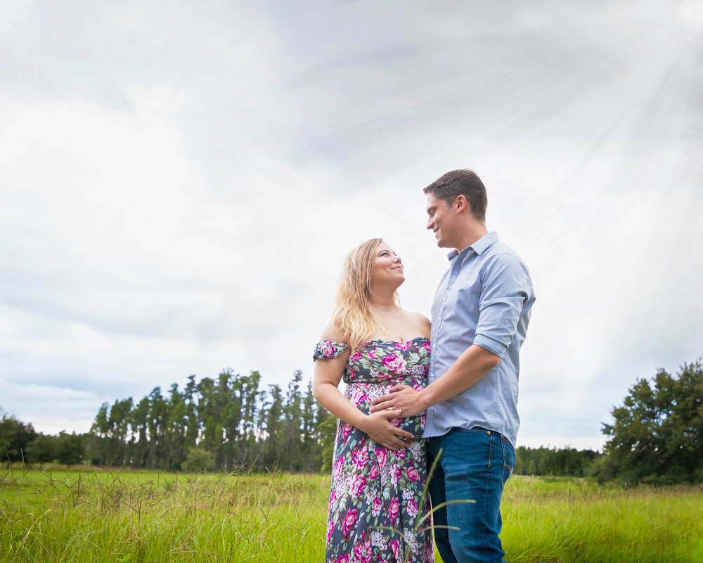 Pregnant couple smile at each other in field with sun rays coming down Wesley Chapel