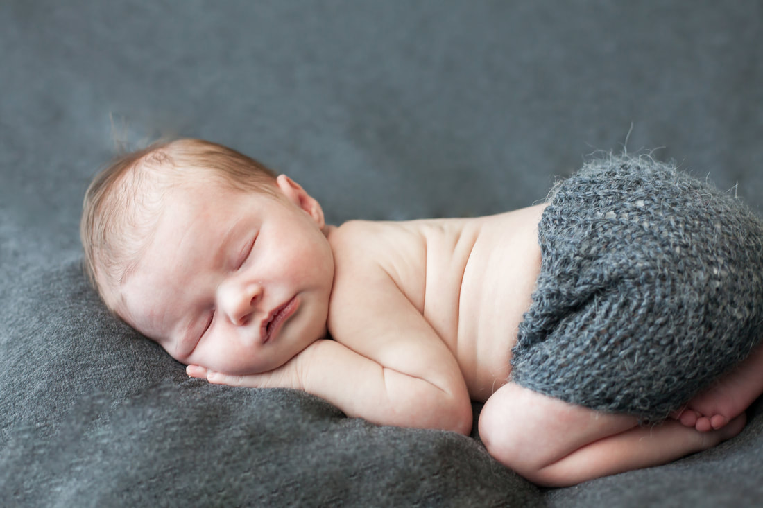newborn baby in grey knit shorts sleeps on her tummy
