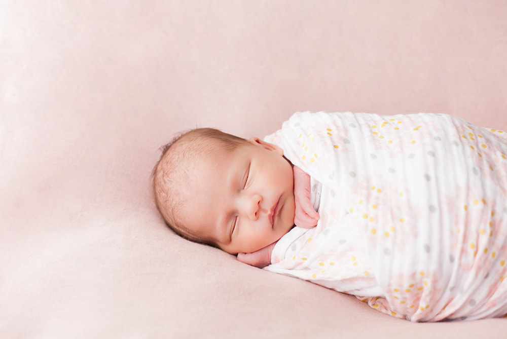 simple sweet photo of a swaddled newborn baby on a pink background. 