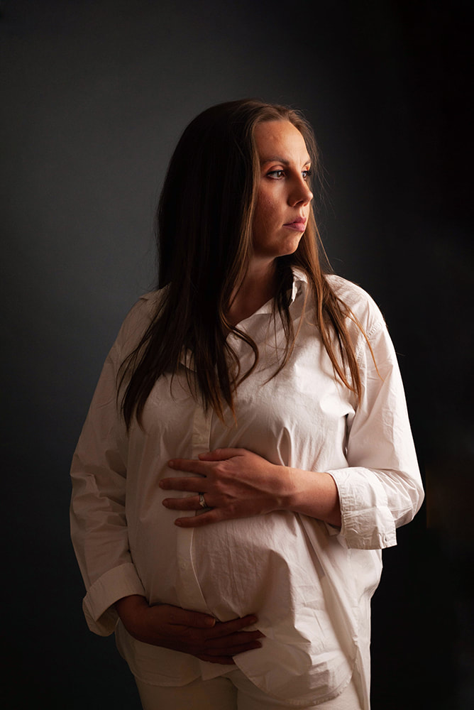 Pregnant Mother looks off toward a light with her hands on her belly 
