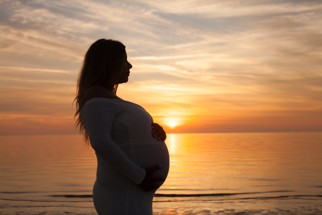 Silhouette of pregnant woman in front of beautiful golden sunset and water