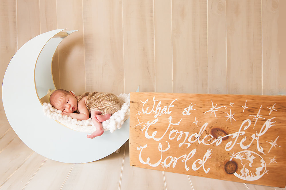 newborn baby boy lies on the moon with a sign next to him that says What a wonderful world