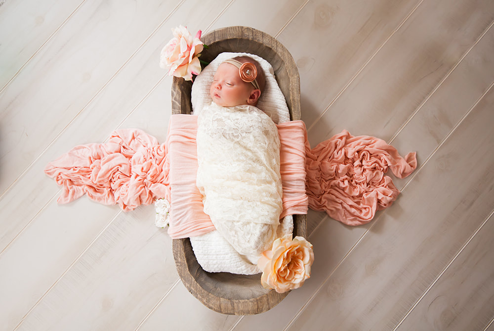 Newborn Photo of a newborn baby swaddled and lying in a long wooden bowl