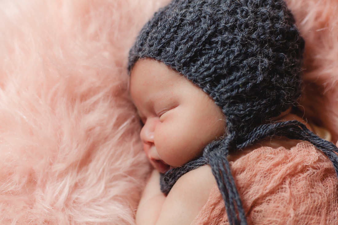 close up of chunky cheeked baby girl in a grey bonnet lying on pink fur