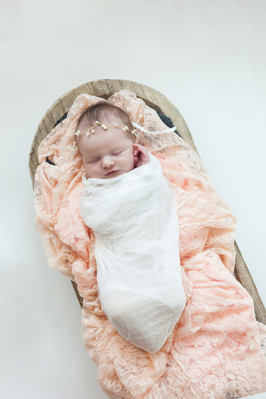 newborn baby girl swaddled in white sleeps peacefully on pink lace