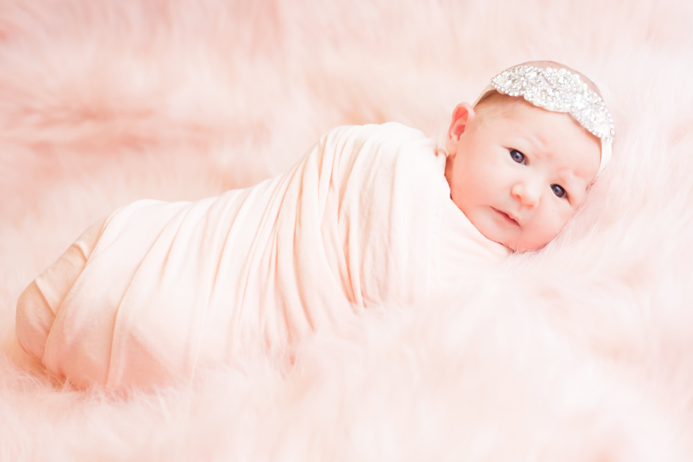 newborn baby swaddled in pink on a pink fur background 