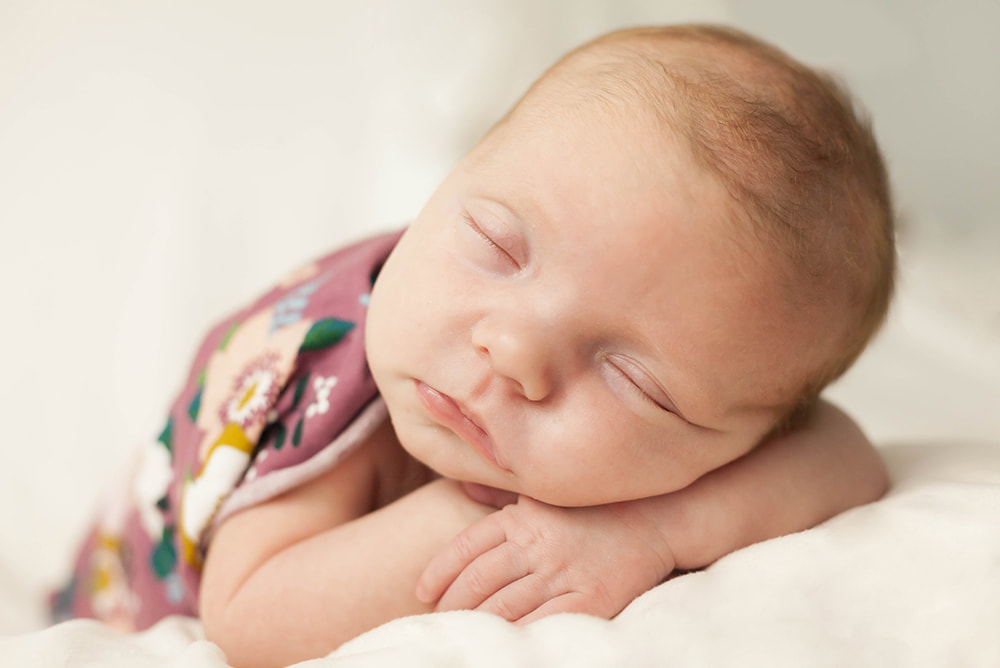 Sleeping baby girl lies on her belly with her hands under her head