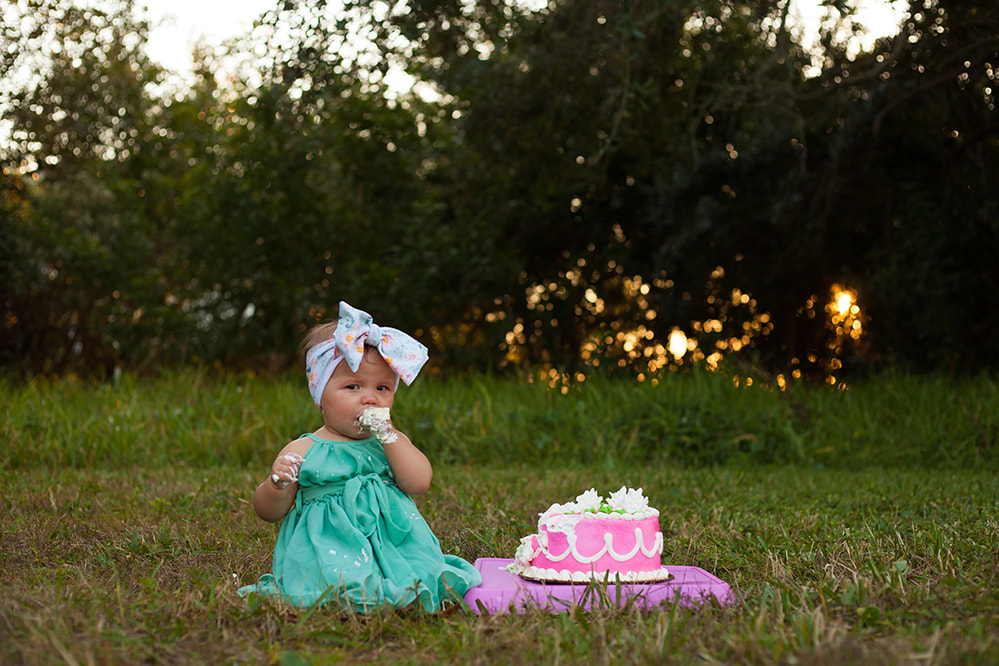 Baby girl in the grass at sunset eating a big handful of cake