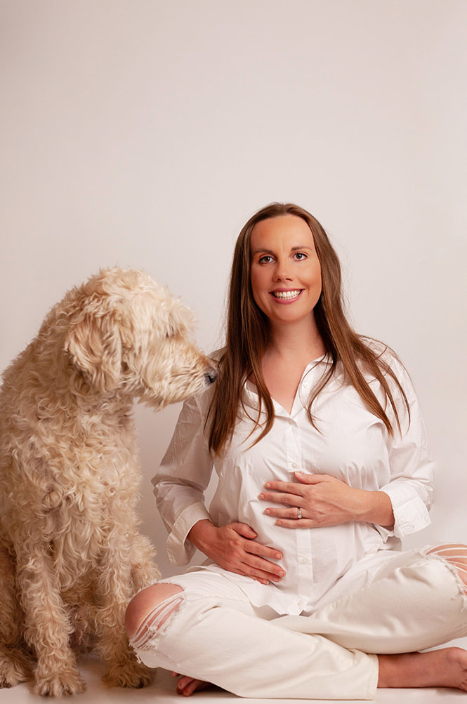 Pregnant Woman sits cross legged on the floor with a big white shaggy dog
