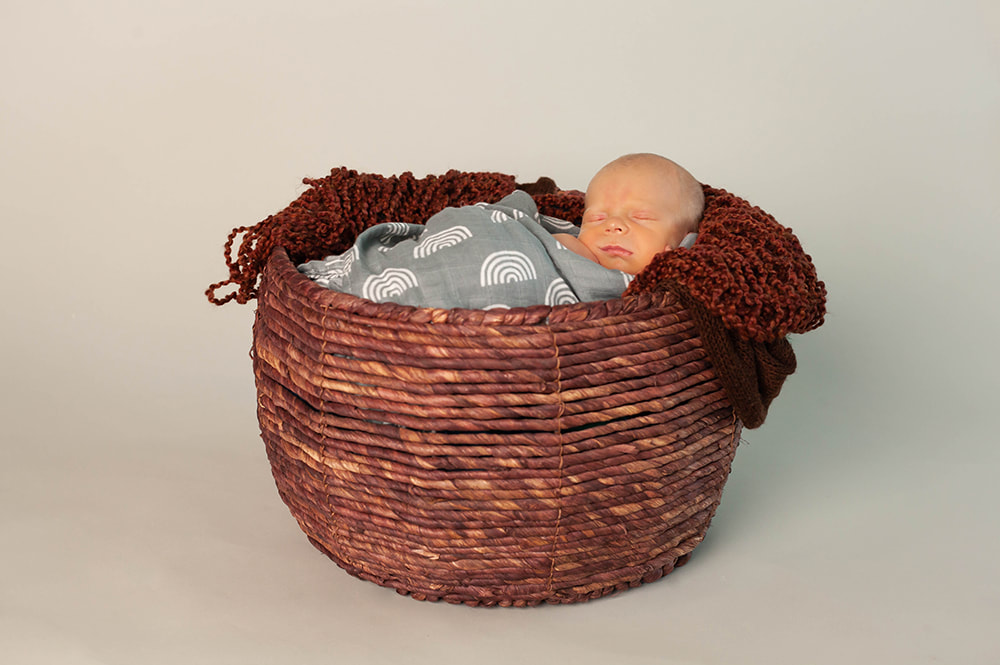 Newborn baby sleeping in wooden basket while swaddled