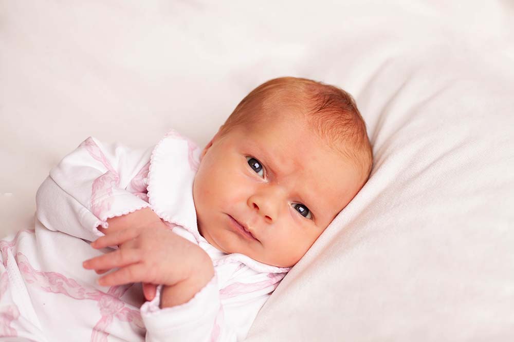 Newborn baby girl looks into camera. White and pink outfit on white background