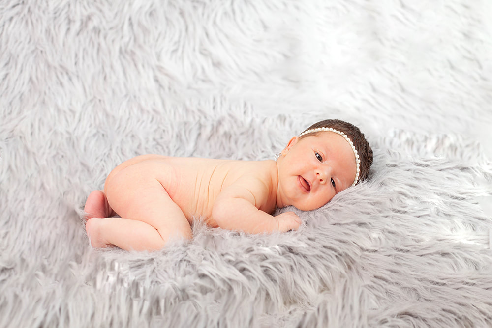 a newborn baby girl looks into camera while lying on light gray fur