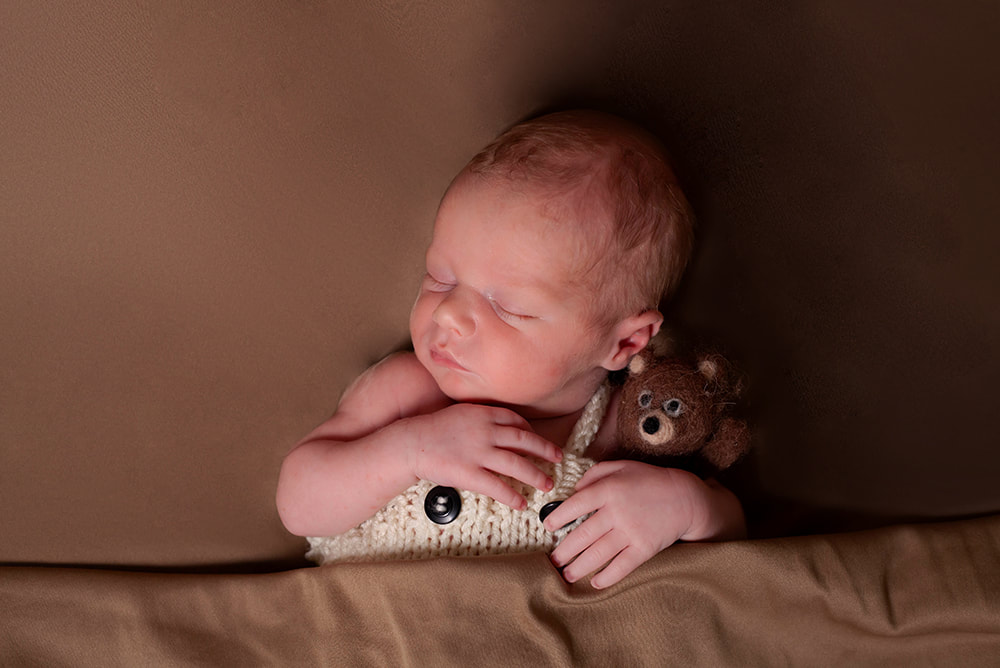 newborn baby boy sleeps tucked it to blanket with a teddy bear tucked into his arm