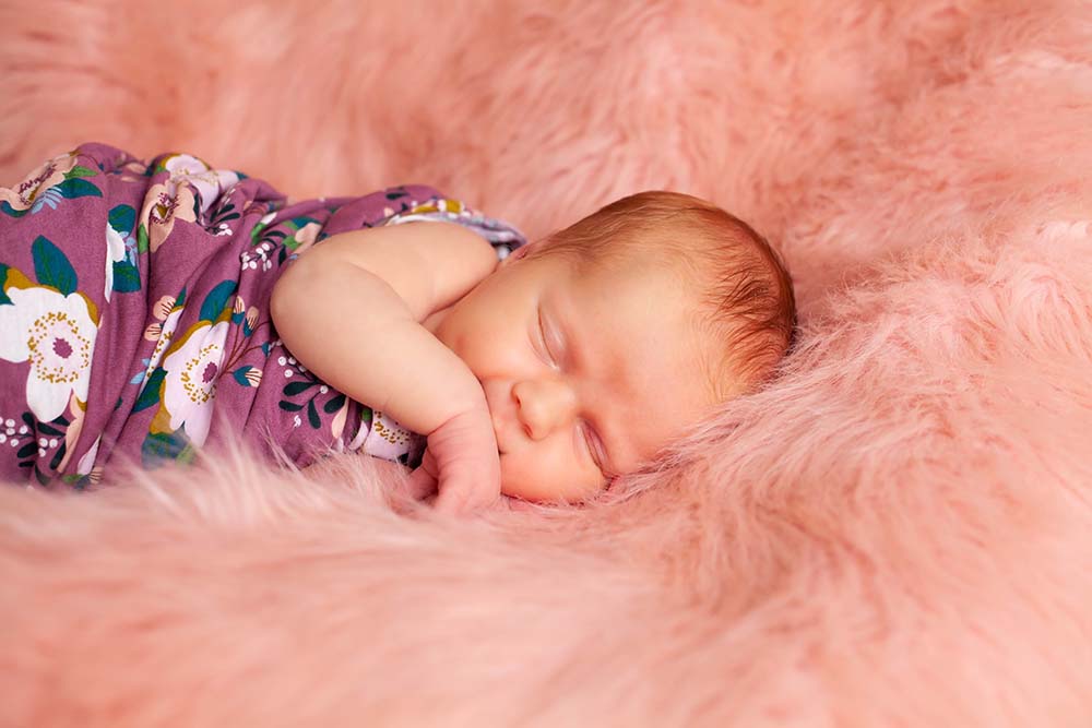 Newborn baby girl lying on pink fur 