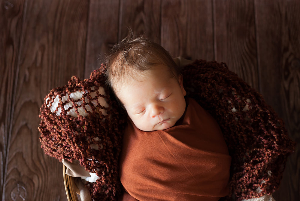 Swaddled newborn baby boy in a basket sleeping