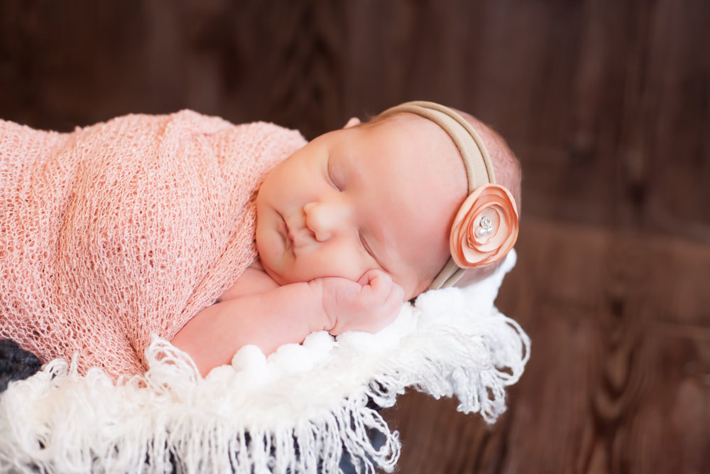 newborn baby sleeping on her side in soft blankets with a dark wood background