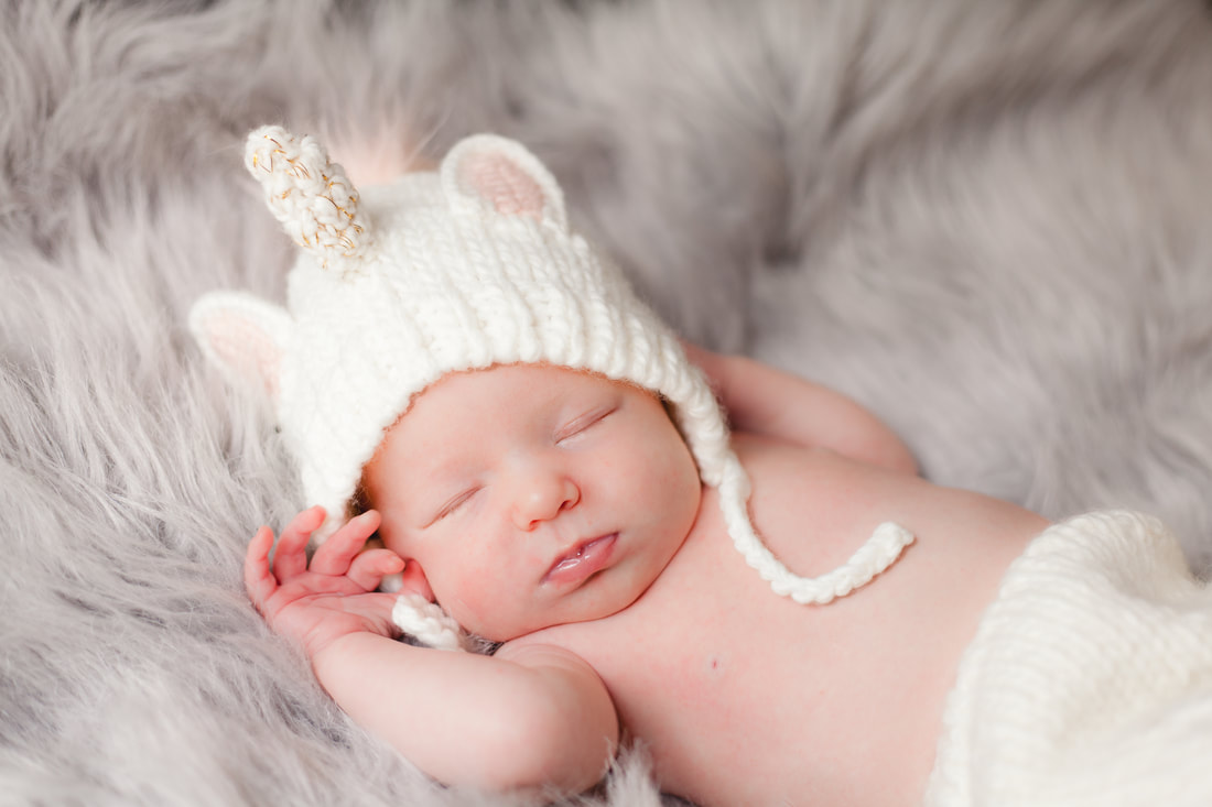 newborn baby girl wearing a unicorn outfit sleeps with her hands up near her face