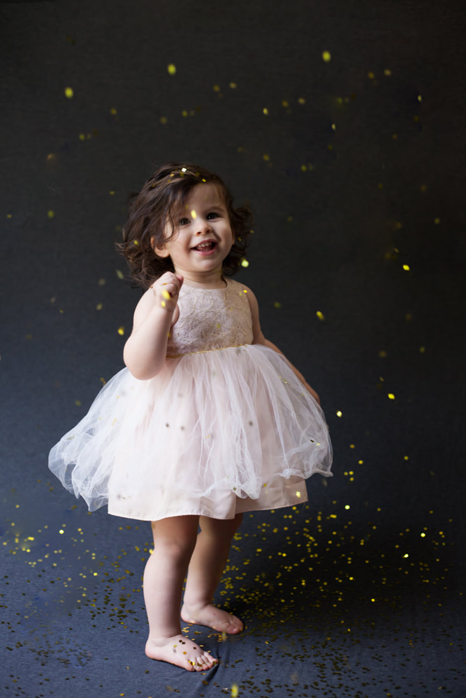 Standing baby smiles at the camera as confetti falls around her
