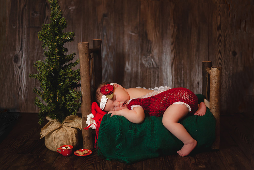 Christmas photo of newborn baby girl lying on a rustic wooden bed with a small christmas tree beside her