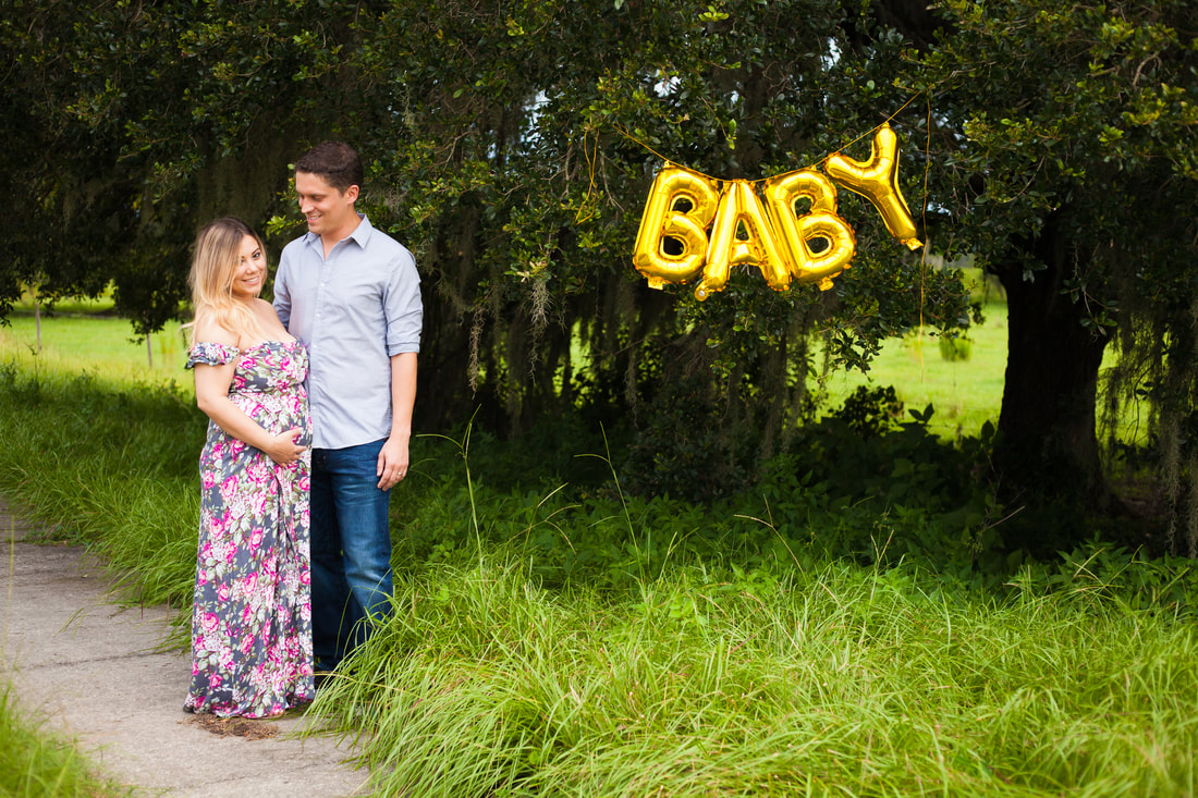 Couple's pregnancy announcement Photo on sidewalk with balloons spelling BABY in tree